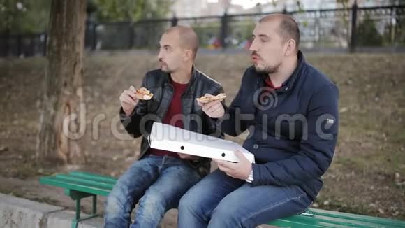两个男人的朋友坐在公园的长凳上从盒子里吃披萨视频的预览图