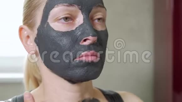 那个女人把泥面罩戴在脸上你的面部护理泥浆水疗程序日间水疗中心在人身上画一个黑色面具视频的预览图
