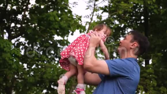 年轻的爸爸和宝宝在户外玩耍时一起笑女孩在父母手边跳着微笑着慢慢视频的预览图