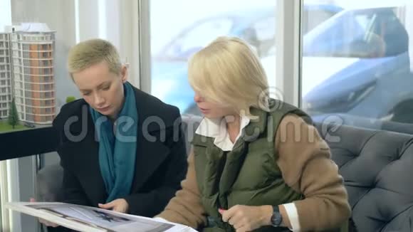 两个女人正在说话坐在售楼处的背景上布置着大楼视频的预览图