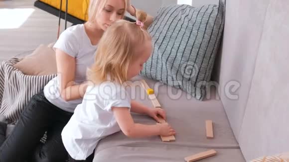 小可爱的金发女孩和她妈妈在沙发上木块从木块走的路视频的预览图