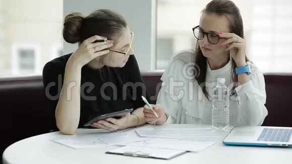 两个商务女性拿着文件工作一台笔记本电脑和一台平板电脑坐在桌子旁商务会议两个伙伴视频的预览图