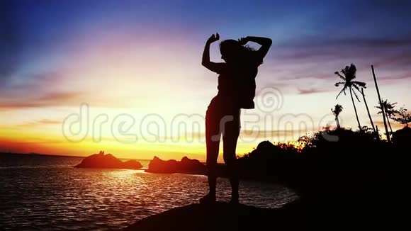 年轻女子在美丽的夕阳下跳舞的剪影矗立在岩石上慢动作1920x1080视频的预览图