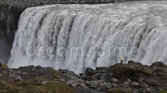 一个年轻的女人欣赏一个强大的狂暴瀑布沿着岩石边缘重重地落下一条晶莹清澈的冰川水流视频的预览图