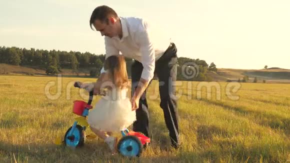 快乐的父亲教小女儿骑自行车爸爸在草坪上和小孩玩孩子学骑自行车视频的预览图