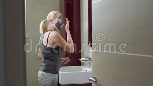 那个女人把泥面罩戴在脸上你的面部护理泥浆水疗程序日间水疗中心在人身上画一个黑色面具视频的预览图