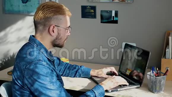 英俊的年轻自由职业者带着眼镜和黄色头发在家工作使用笔记本电脑时尚的成功男人视频的预览图