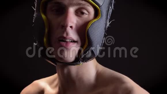 一个年轻的白种人赤裸上身的男性疲惫拳击手的肖像戴着拳击头盔头戴护头看着镜头黑色视频的预览图
