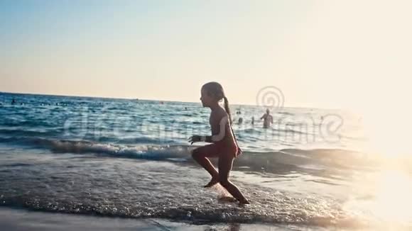一个赤脚的小女孩在晚阳的温暖光线下沿着大海在潮湿的沙子上奔跑的缓慢运动粗心和粗心视频的预览图