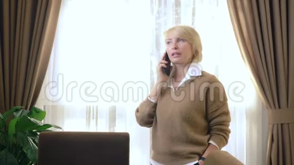 美丽的女人在用手机说话站在窗边的办公室里视频的预览图