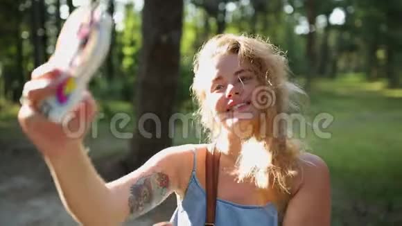 穿着漂亮的欧洲女人在日落时分在森林里用手机自拍和发短信在户外自拍视频的预览图