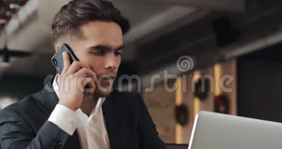 穿着紧身的年轻商人手提电脑在咖啡馆工作3他和老板打电话把电话记在嘴边视频的预览图