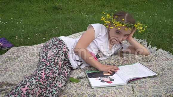 头戴花圈的可爱女孩在看书躺在草地上的孩子视频的预览图