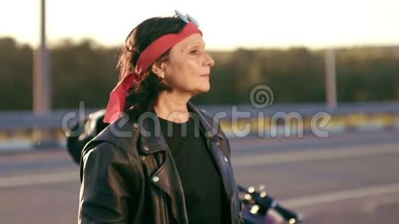 一位穿着皮夹克和手套的老妇人站在一条空路的背景下女人把手放在视频的预览图