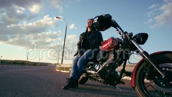 一个穿着皮夹克和手套坐在一辆摩托车上的老年骑自行车的女人在一条空路的背景下这就是视频的预览图