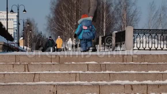 令人认不出的孩子和冬天的公园里和他的父亲一起走在雪梯旁视频的预览图