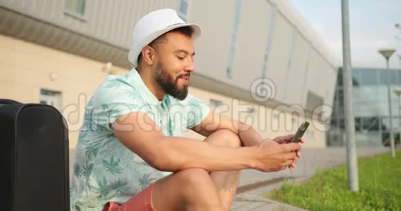 准备度假的非洲男人正坐在街上一边聊天一边在手机上浏览视频的预览图