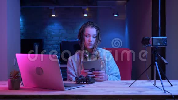 年轻有魅力的女性博客写手戴着可怕的耳机用平板电脑和平板电脑进行现场直播视频的预览图