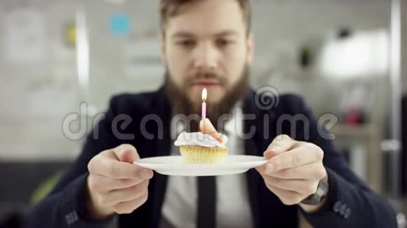 胡子商人上班族在办公室里庆祝一个孤独的生日他在一个小蜡烛上吹蜡烛视频的预览图