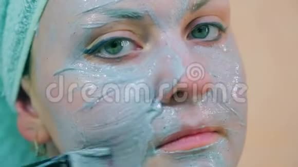 一个微笑的女人的脸头上有一条毛巾皮肤上有一刷蓝色的粘土特写视频的预览图