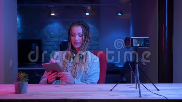 使用平板电脑和平板电脑进行现场直播这是一位年轻有魅力的女性博客写手带着可怕的耳机的特写镜头视频的预览图