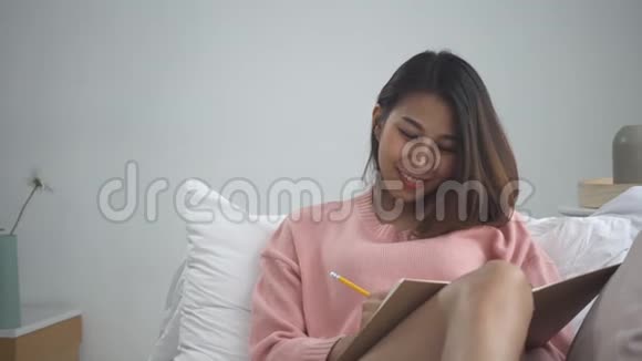 快乐的亚洲年轻女性在家学习在家中躺在沙发上微笑在手机上看短信或短信视频的预览图