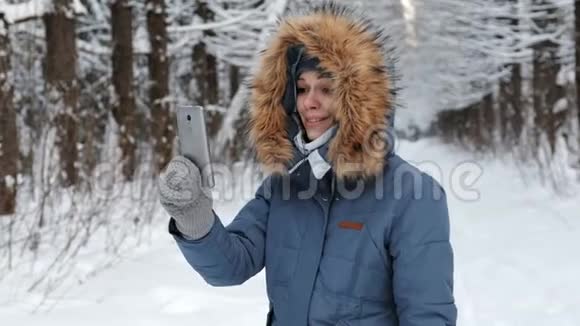 冬日公园里一位穿着蓝色夹克头戴皮帽的美女在用手机聊天视频的预览图