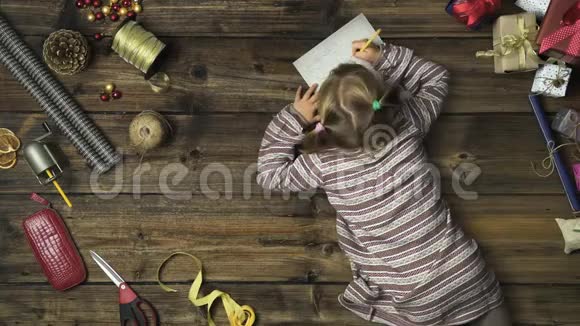 头顶上的女孩在老式木桌上写圣诞老人的信而妈妈则在用手工艺品准备礼品盒视频的预览图