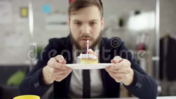 悲伤的胡子商人办公室工作人员正在办公室里庆祝一个孤独的生日他在一个小蜡烛上吹蜡烛视频的预览图
