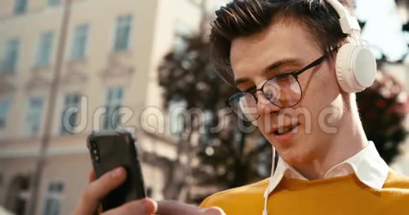 侧面肖像一个戴眼镜的年轻金发男子正在用手机聊天浏览和发短信视频的预览图