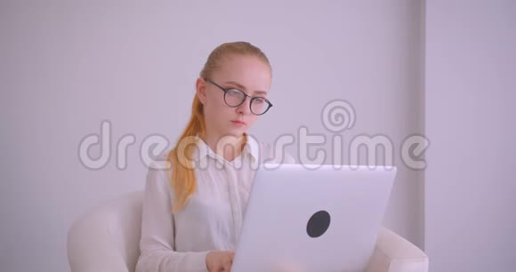 年轻漂亮的白种人金发女商人戴商人戴着眼镜用手提电脑看着坐在里面的照相机视频的预览图