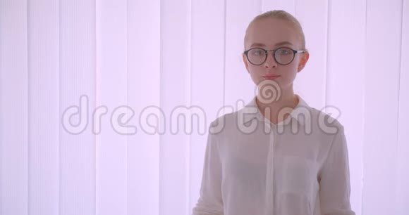 年轻漂亮的白种人金发女学生戴着眼镜看着摄像机站在室内视频的预览图