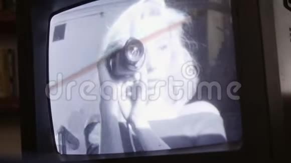 一个漂亮的金发女孩手里拿着小相机在老式电视上播放视频的预览图