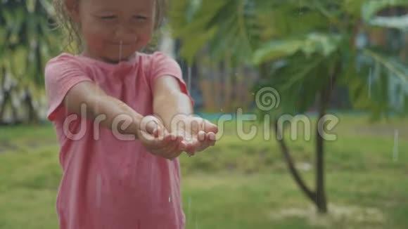 一幅5岁的小女孩在热带雨中嬉戏慢动作的肖像视频的预览图