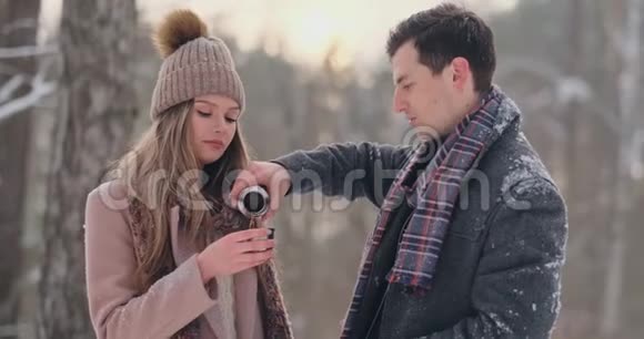 一对相爱的夫妇在冬天的森林里喝热水瓶里的茶穿外套的时髦男女视频的预览图