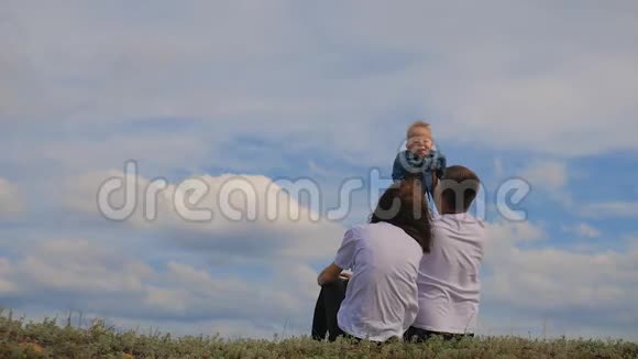 幸福的一家人坐在绿草上家庭在户外玩得很开心快乐的年轻家庭在一起视频的预览图