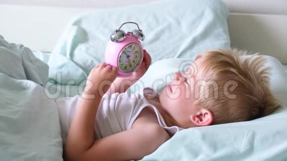 一个金发小男孩躺在床上微笑一大早就玩闹钟那男孩听着钟响视频的预览图