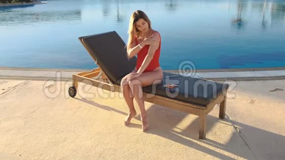 穿红色泳装的迷人女孩在晒黑的皮肤上涂上防晒霜以保护皮肤防止阳光下的衰老视频的预览图