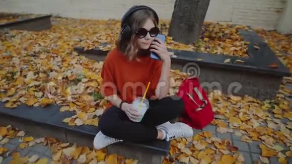近距离欣赏时尚的年轻人戴着耳机听音乐喝着奶昔从一个塑料杯走在街上视频的预览图