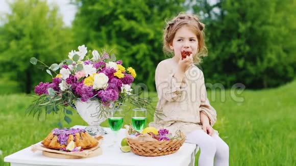 可爱的小女孩穿着一件明亮的智能连衣裙坐在桌子上用巧克力糖果吃手圣帕特里克日野餐视频的预览图