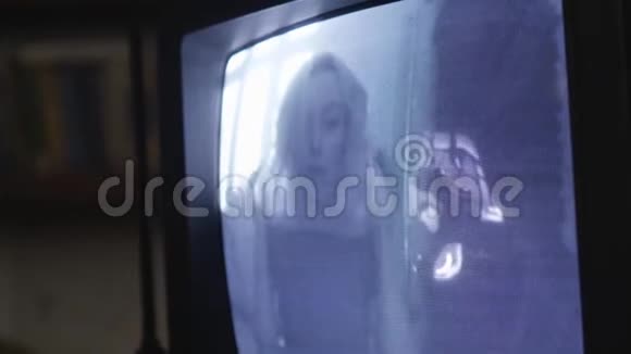 后面有窗户的金发女孩出现在旧电视机的屏幕上向下看视频的预览图