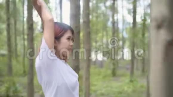 健康美丽的年轻亚洲运动员穿着运动服装双腿发暖手臂准备在森林里奔跑视频的预览图