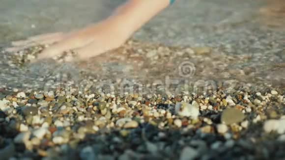 一个女人她的手在寻找大海边缘浅卵石中的东西视频的预览图