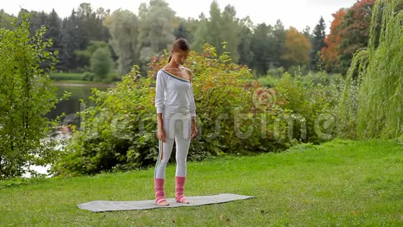 年轻苗条的漂亮女人在湖边的公园里做颈部健康的健身运动视频的预览图