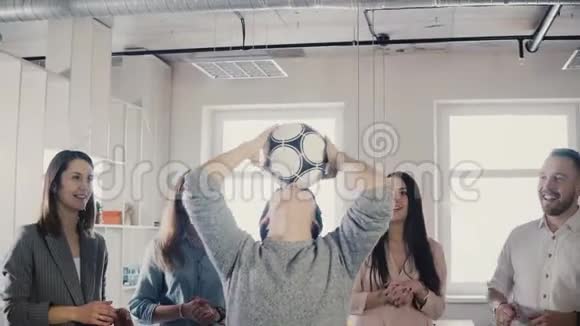 一个快乐的亚洲男人试图在头上玩足球积极的混血儿在办公室玩有趣的运动游戏4K视频的预览图