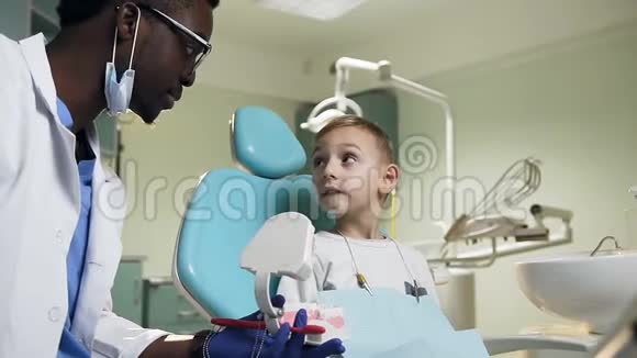 非洲男性牙医向小男性病人展示塑料牙齿模型视频的预览图