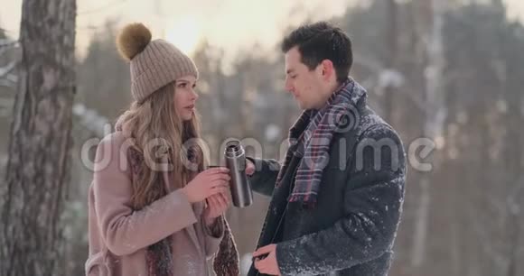 一对相爱的夫妇在冬天的森林里喝热水瓶里的茶穿外套的时髦男女视频的预览图