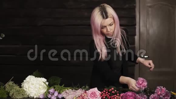 一个年轻的女孩花店清洁一朵粉红色的康乃馨花各种各样的花黑暗的背面视频的预览图