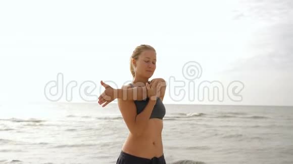 年轻女子在海滩上放松和日光浴美丽的女人在做瑜伽站在沙滩上摆出海景视频的预览图