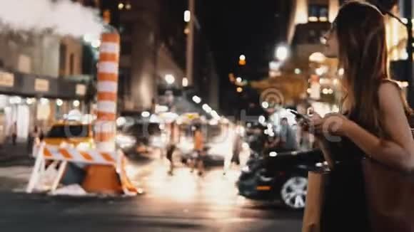 年轻的美女晚上穿过美国纽约市中心的交通道路使用智能手机视频的预览图
